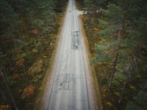 Suomalainen metsätie kiemurtelee tiheän mäntyjen keskellä, syksyiset värit ja kulunut asfaltti näkyvissä ylhäältä